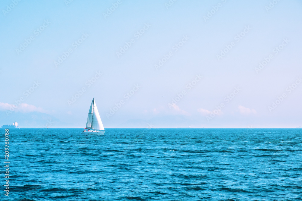 Lonely sailing boat with white sails in open sea. Beautiful romantic landscape, seascape. Luxury sports and recreation background. Horizontal image with copy space. 