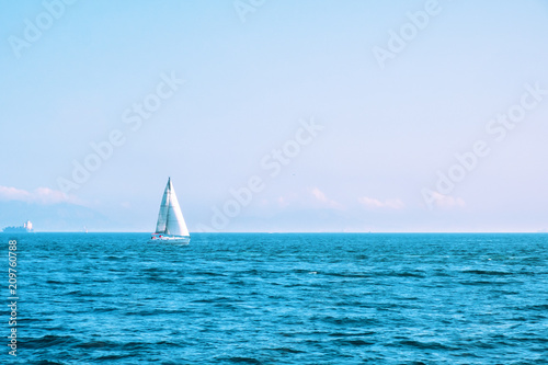Lonely sailing boat with white sails in open sea. Beautiful romantic landscape, seascape. Luxury sports and recreation background. Horizontal image with copy space. 