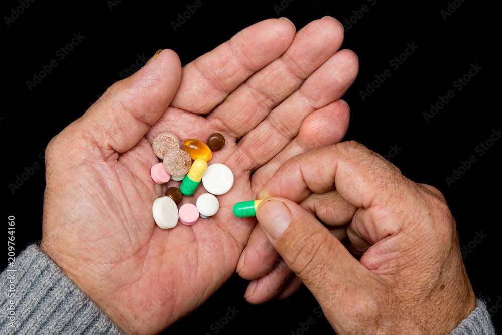 An elderly man holds a lot of colored pills in old hands on a dark background. Painful old age. Health care of older people. Top View An elderly man holds a lot of colored pills in old hands on a dark background. Painful old age. Health care of older people. Top View