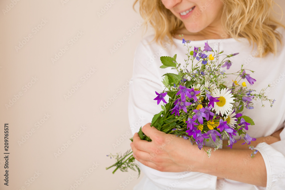 Closeup of woman's hands holding beautiful bunch of wild flowers. Girl with summer bouquet at white wall Closeup of woman's hands holding beautiful bunch of wild flowers. Girl with summer bouquet at white wall