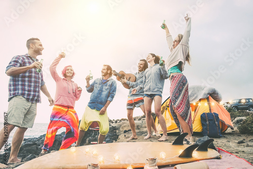 Happy friends dancing and having fun making a beach party in the campsite - Young people laughing and drinking beers while camping next ocean - Travel, vacation, lifestyle concept