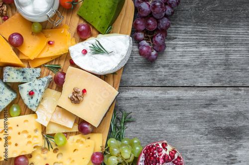Assorted cheeses on wooden board plate served with walnuts, grapes, pomegranate and rosemary