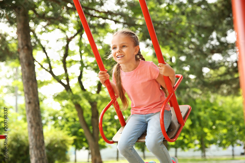 Cute little girl playing on swings in park