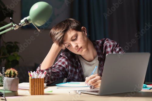Teenager doing homework at table in evening photo