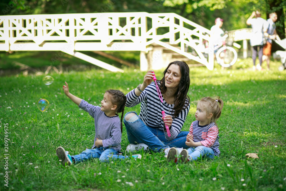 Fototapeta premium Happy mother and daughters in the park. Beauty nature scene with family outdoor lifestyle.