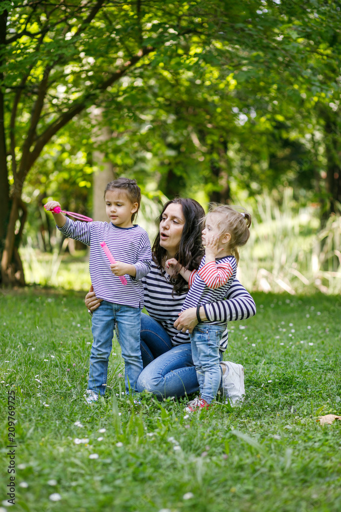 Fototapeta premium Happy mother and daughters in the park. Beauty nature scene with family outdoor lifestyle.