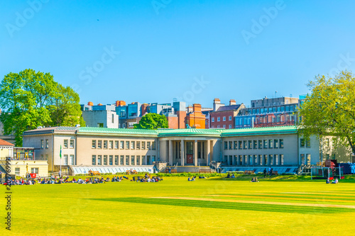 Students are having a picnic on a field inside of the trinity college in Dublin, Ireland