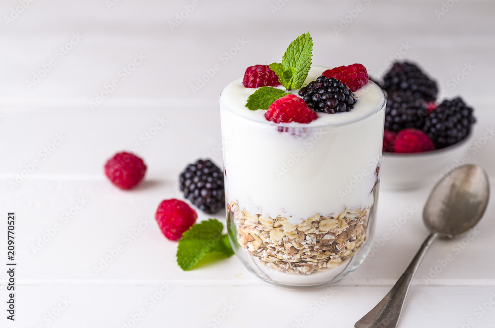White yogurt with muesli and raspberries in glass bowl on white wooden background. White yogurt with muesli and raspberries in glass bowl on white wooden background.
