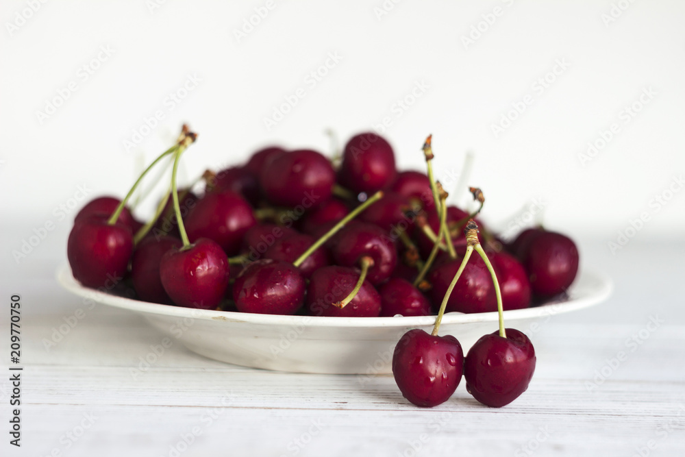 Ripe cherry berries with water droplets on a white plate on a white wooden background, clean, healthy and tasty fruit. Ripe cherry berries with water droplets on a white plate on a white wooden background, clean, healthy and tasty fruit.