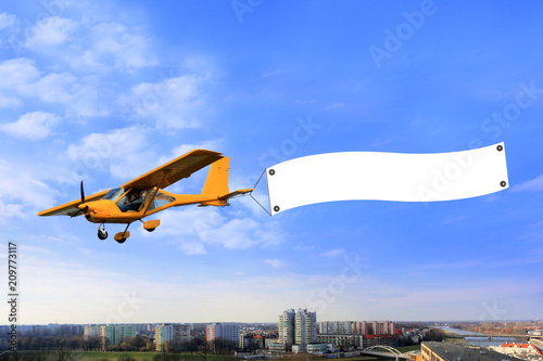 Reklama lotnicza, samolot awionetka z bilbordem reklamowym nad miastem.