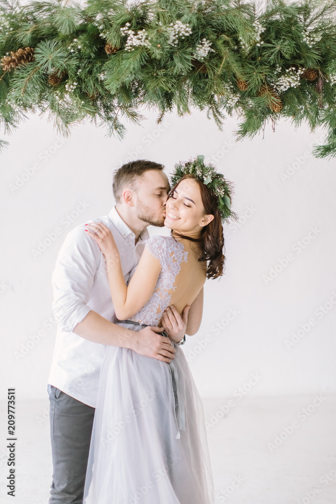 Beautiful bridesmaid in pine wreath and gray blue dress with handsome groomsman in the studio hugging.