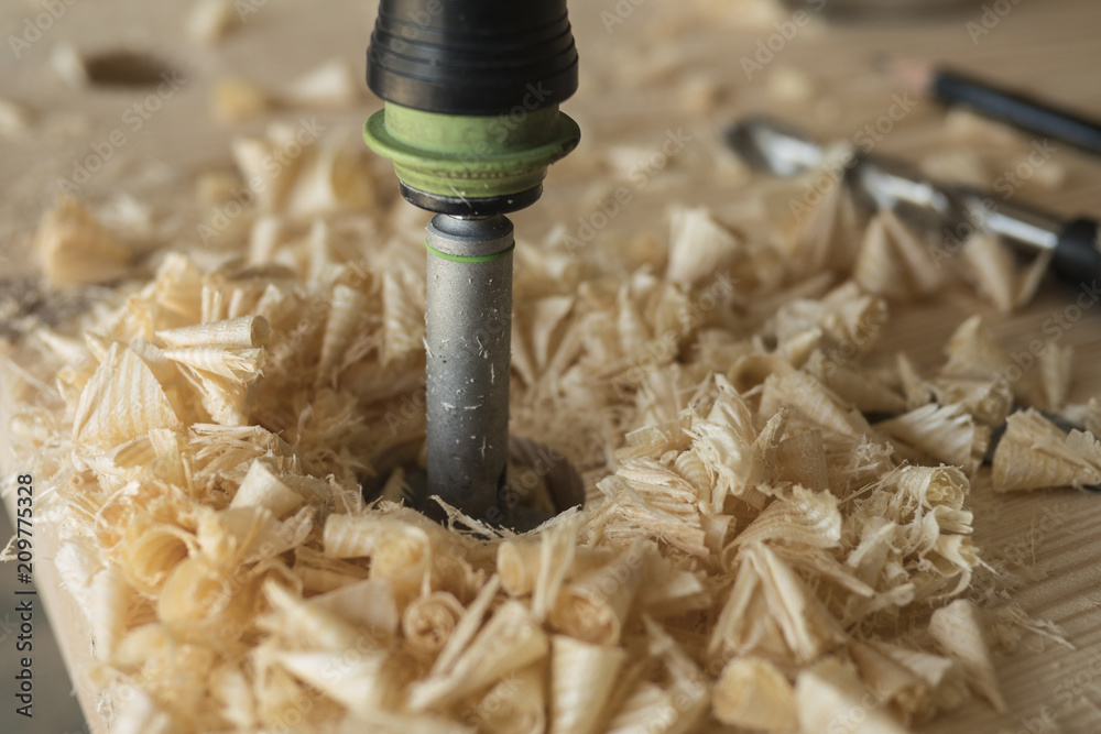 The joiner drills a workpiece of wood with a drill. A drill, a pencil and a corner The joiner drills a workpiece of wood with a drill. A drill, a pencil and a corner