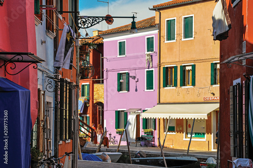 View of colorful buildings, people and boats in front of a canal at Burano, a gracious little town full of canals, near Venice. In the Veneto region, northern Italy © Celli07