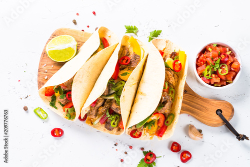 Mexican pork tacos with vegetables and salsa on white.