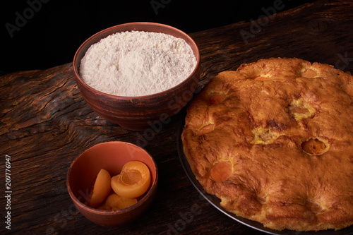 A bowl with flour and apricot cake on a wooden background photo