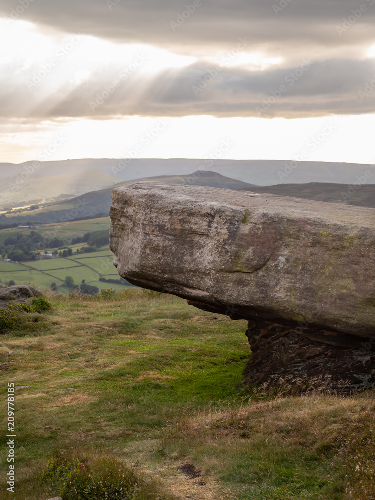Rock formation near stanage edge in the peak district of great britain with columns of light shining through the clouds