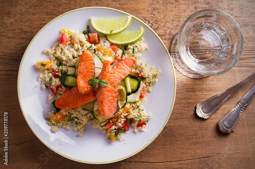 Roasted salmon fish with tomato couscous, zucchini and lime on white plate. overhead, horizontal