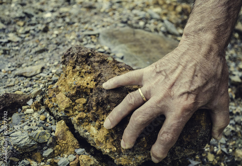 Senior person hand lifting a stone from the ground with the colors of the mineral