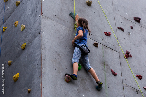 Beautiful young girl climbing to big artificial wall