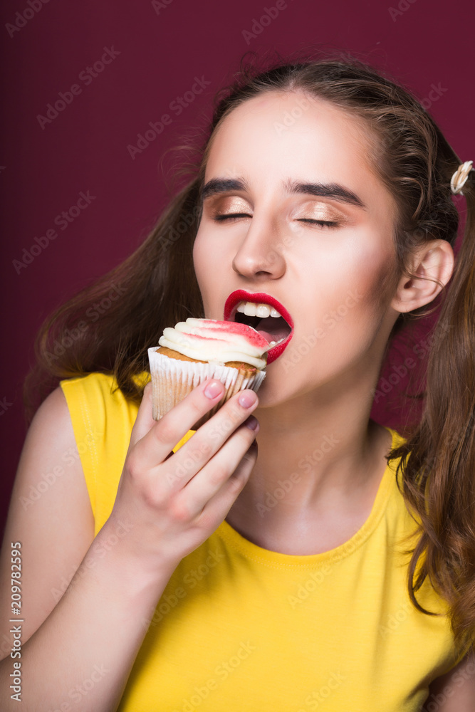 Hungry brunette model biting yummy cake with cream over a red background