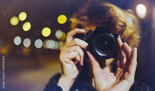 Hipster hiker tourist making photo, holding in hands camera on background of evening atmospheric city, blogger view in holiday, photographer girl enjoying night street, traveler relax 