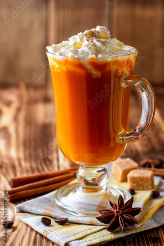 Pumpkin spice latte with whipped cream and cinnamon in glass on rustic wooden background