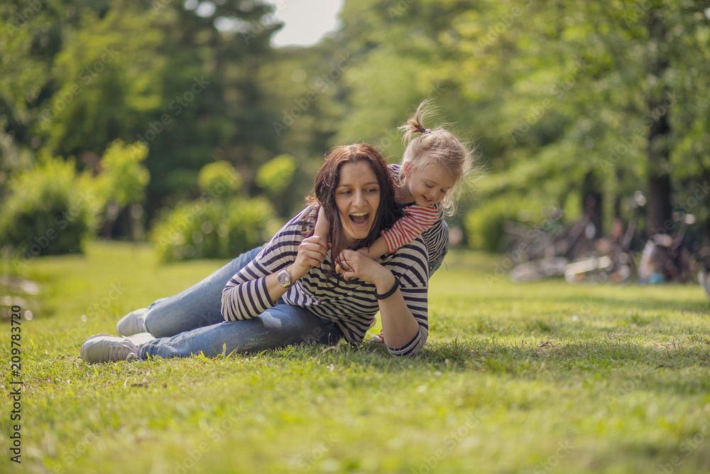Happy mother and daughter in the park. Beauty nature scene with family outdoor lifestyle. Happy family resting together on the green grass, having fun outdoor. Happiness and harmony in family life Happy mother and daughter in the park. Beauty nature scene with family outdoor lifestyle. Happy family resting together on the green grass, having fun outdoor. Happiness and harmony in family life