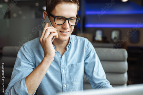 Portrait of a young man with a good mood, a businessman in a shirt and glasses, who works on a laptop and talking on the phone in a cafe, can be used for advertising, text insertion.