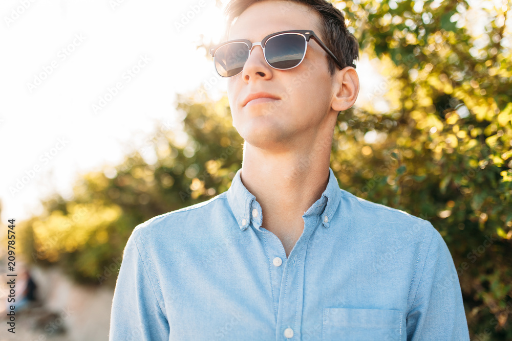 Beautiful stylish guy with glasses, posing on the beach, at sunset, hipster posing in stylish clothes, for advertising, text insertion