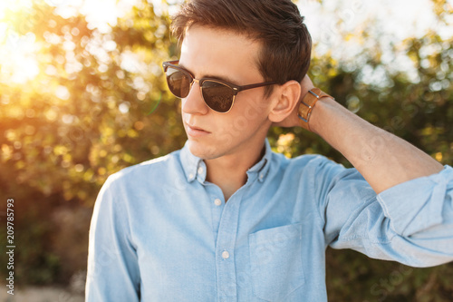 Beautiful stylish guy with glasses, posing on the beach, at sunset, hipster posing in stylish clothes, for advertising, text insertion