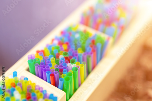 Bunch of colorful plastic sipping straws in wooden box at cafe counter. Drinks decoration and accessories. Bright multicolored background