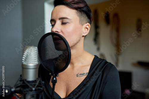 Beautiful sensual woman singing in music recording studio standing near microphone with eyes closed.  © Seventyfour