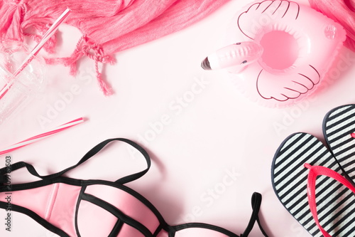 Beach pink background. Swimsuit, flip flops, pink flamingo toy. Summer and beach objects theme on a light background. Flat lay, top view, copy space 