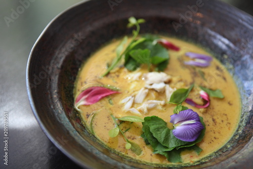 Beautiful and colorful bowl of Thai crab curry garnished with edible flowers at professional Starred restaurant. Modern concept style of Food Styling, creative plating and decorating presentation idea