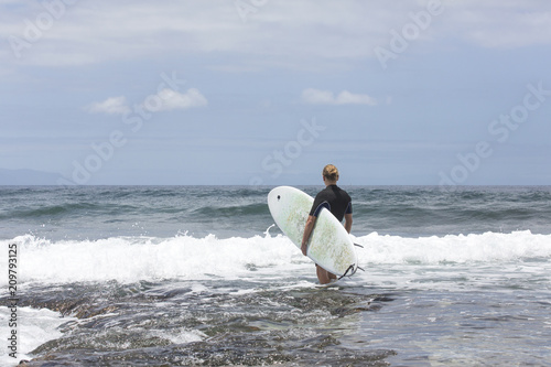 The surf enters the water. Male surfer entering the sea with his board in a black surfing suit. Tenerife, Spain. Surfer entering the ocean .Ready for a great surfing day.