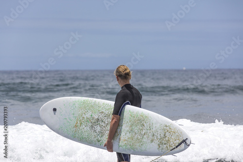 The surf enters the water. Male surfer entering the sea with his board in a black surfing suit. Tenerife, Spain. Surfer entering the ocean .Ready for a great surfing day.