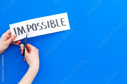 All is possible concept. Hands cutting the part im of written word impossible by sciccors. Blue background top view copy space