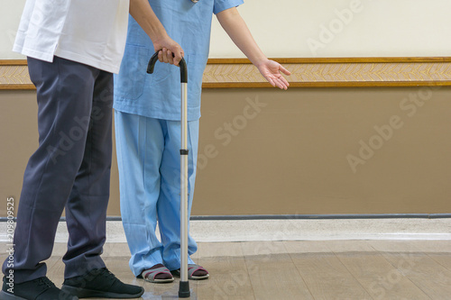 Medical and healthcare concept, Physiotherapist in blue attire to take care of the elderly in the clinic, walking stick helps the elderly to walk better.