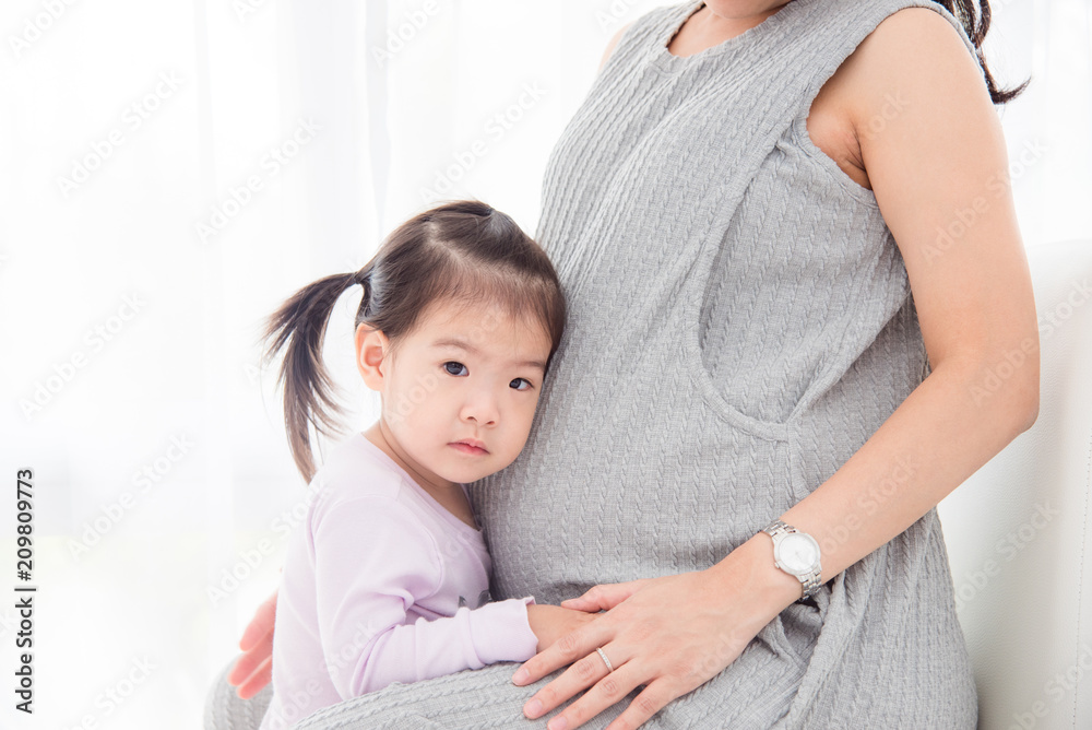 Little Asian girl standing with pregnant mother and doing serious face Little Asian girl standing with pregnant mother and doing serious face