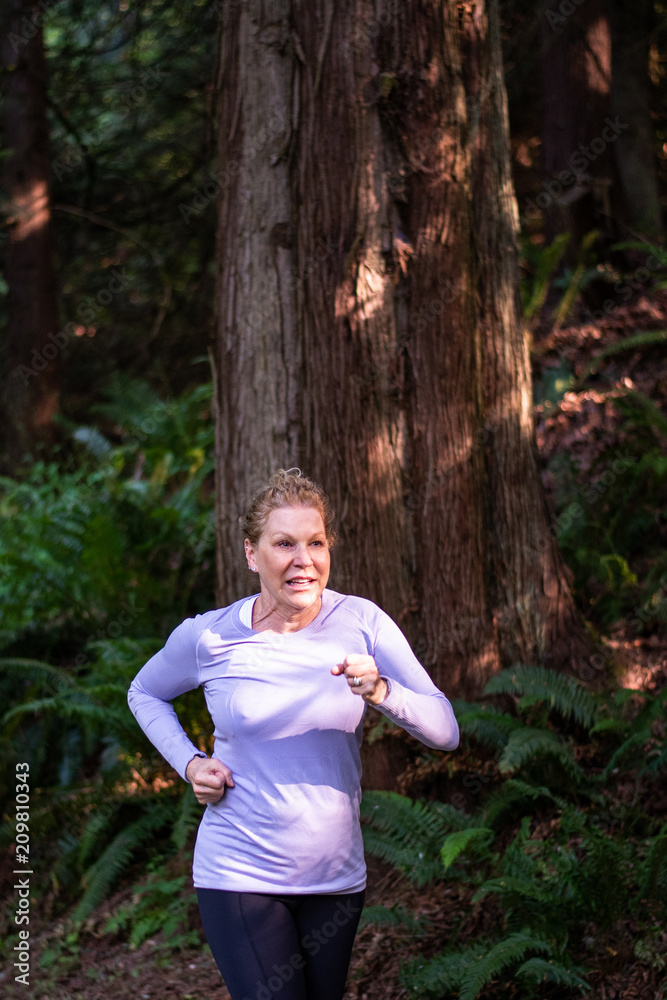 Baby boomer adult woman with blond curly hair, purple shirt, and black pants running in the woods
