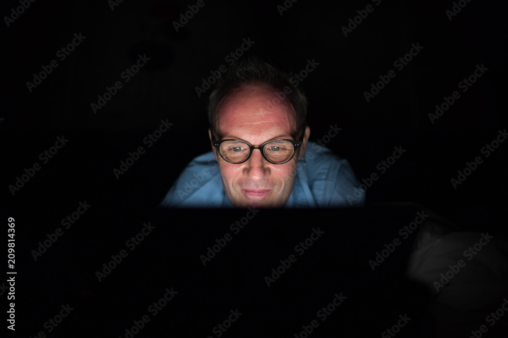 Mature Scandinavian man using digital tablet in dark room Mature Scandinavian man using digital tablet in dark room