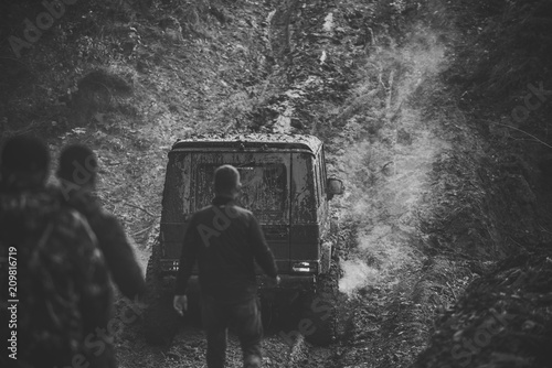 off-road. Company of three men looks at suv drives with smoke.