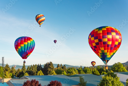 Six Hot Air Balloons Flying Over Rooftops and Treetops Up Into the Sky