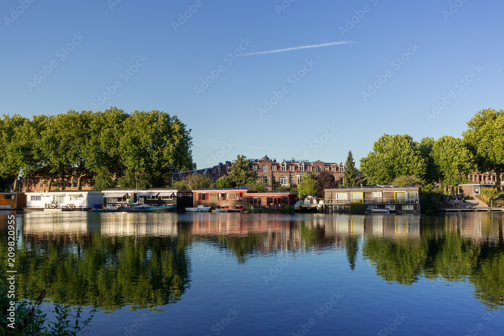 Waterview with mix of elements such as flaoting houses in front of neighbourhood reflected in the water