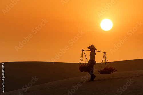 Woman carrying flower basket at sunset in Mui Ne sand dune, Vietnam