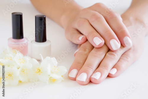 Young  perfect  groomed woman s hands with pink and white nail varnish bottles. Nails care. Manicure  pedicure beauty salon. Beautiful jasmine blossoms on table. Fresh flowers.