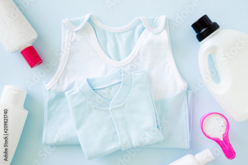 Pink cup or scoop of white powder with liquid bottles on pastel blue table. Different detergents for baby clothes washing. Dry cleaning. Regular washing. Mother and father duties. Daily routine.