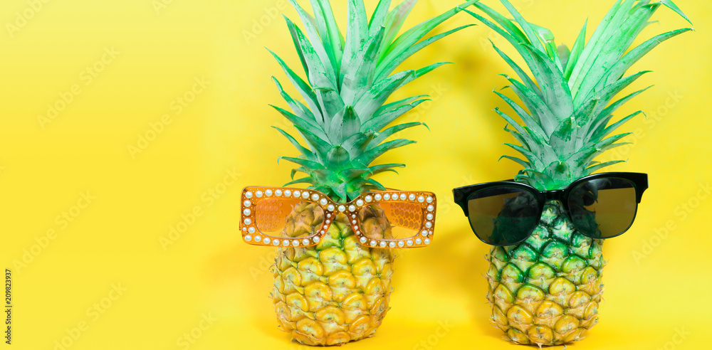 Pineapple wearing sunglasses on a yellow background. Summer and fashion concept.