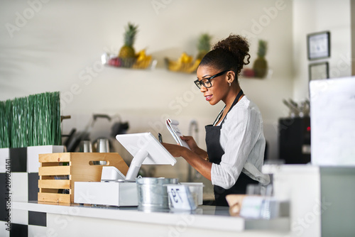 shop assistant placing order from notepad into pos point of sale terminal at register in restaurant
