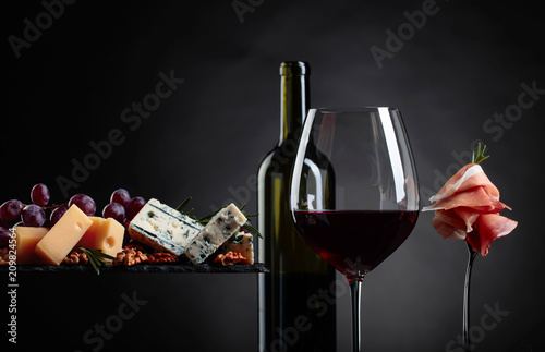 Glass of red wine with various cheeses , fruits and prosciutto.
